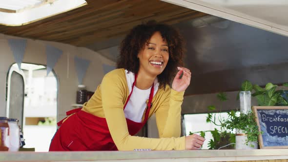 Portrait of african american woman wearing apron smiling while standing in the food truck alt