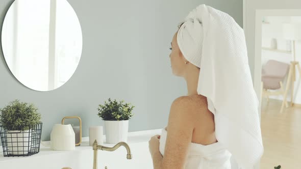 Happy attractive woman looks in bathroom mirror in morning