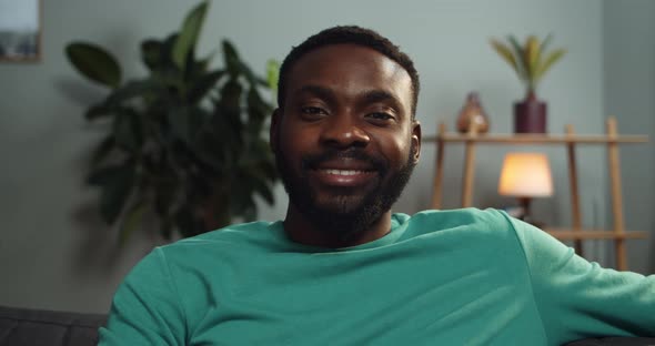Close Up View of Cheerful Guy Sitting on Sofa and Smiling, Portrait of Afro American Man Looking alt
