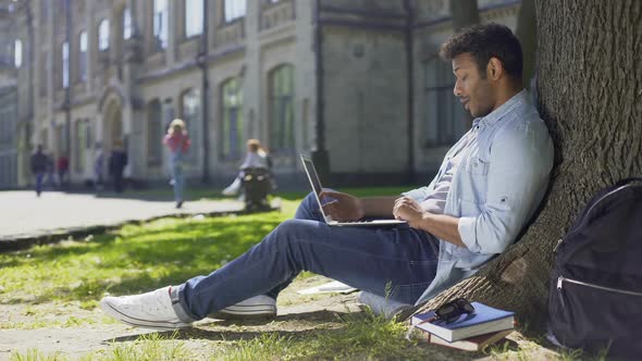 Young Mixed-Race Guy Using Laptop Under Tree, Surprised Reaction, Good News alt