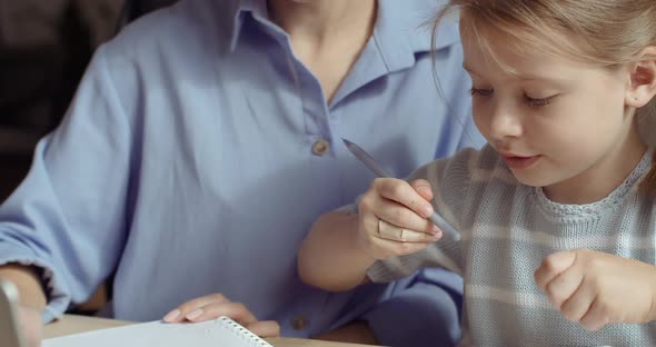 Close-up of Preschool Girl Sitting with Teacher Educator at Table at Home or in Kindergarten, Learns alt