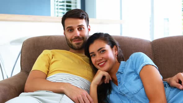 Portrait of smiling couple relaxing on sofa in living room alt