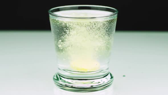 Close-up Shot of An Effervescent Pill Against Pain Falls Into a Glass and Dissolves Slow-motion Shot alt