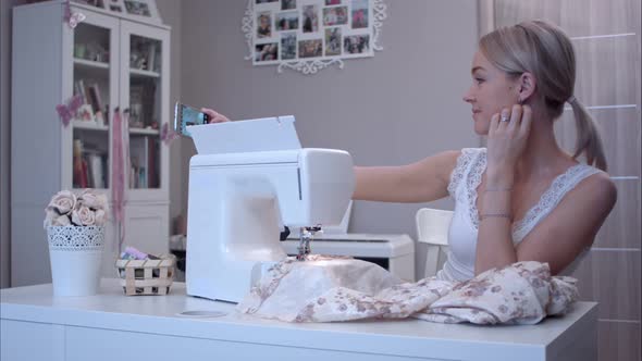 Young Woman Taking Selfies with Her Phone While Sitting Next To Sewing Machine alt
