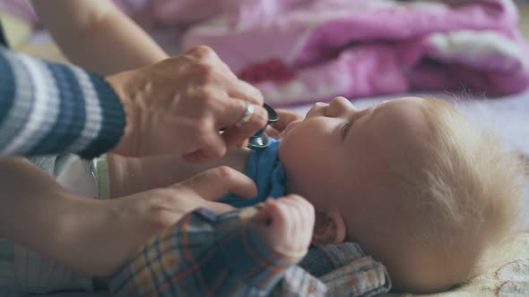 Pediatrician Listens To Baby Lungs with Stethoscope on Bed alt