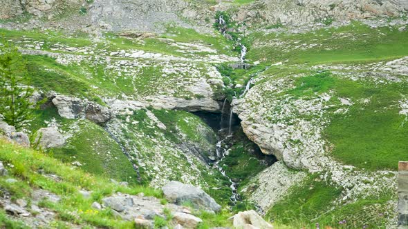 Tilting up towards the rocky peaks above a waterfall in Barcelonnette, France. alt