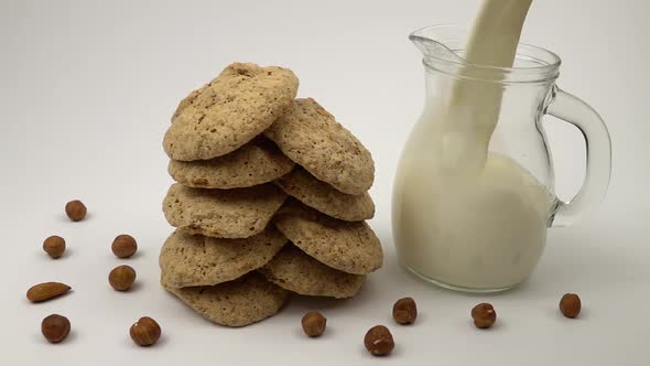 Milk is poured into a glass jug, that standing on the table next to the cookies, slow motion