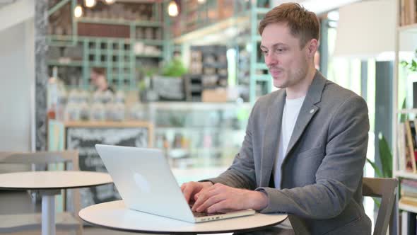 Successful Young Man Celebrating on Laptop in Cafe alt