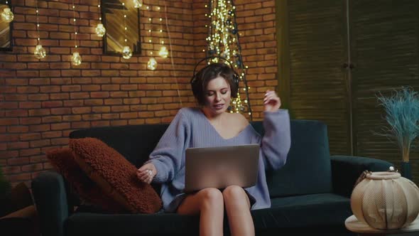 Stylish Girl Uses a Laptop Listens to Music in Headphones Sings and Dances alt