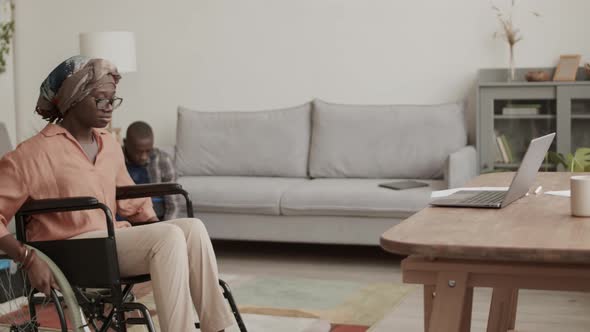 Disabled Woman Working on Computer while Carpenter Assembling Table alt