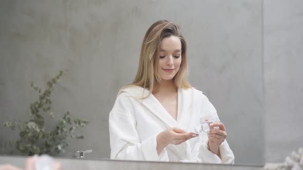 Goodlooking Woman Use Skin Care Products at Home in Light Bathroom