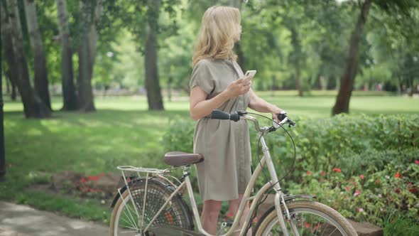 Portrait of Positive Caucasian Middle Aged Woman with Bike Checking Online Map in Smartphone and alt