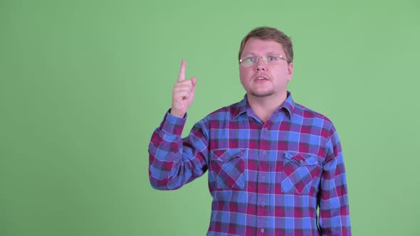 Happy Overweight Bearded Hipster Man Talking While Pointing Up