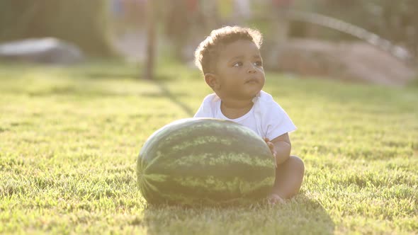 cute dark-skinned kid is sitting on the grass with a watermelon in summer