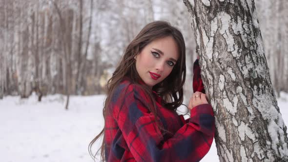 Young Woman with Wavy Hair Standing and Touching Face in Winter Forest