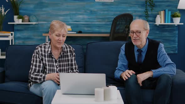 Smiling Senior Couple Looking at Laptop Computer Waving During Videocall alt