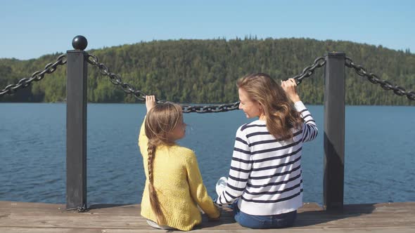Mother and Daughter Sitting on Pier Warm Autumn Day alt