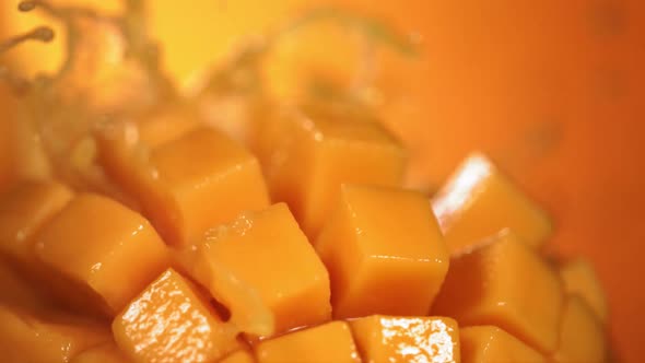Slow Motion Shot of Mango Juice Splashing Through Mango Cube Slices alt