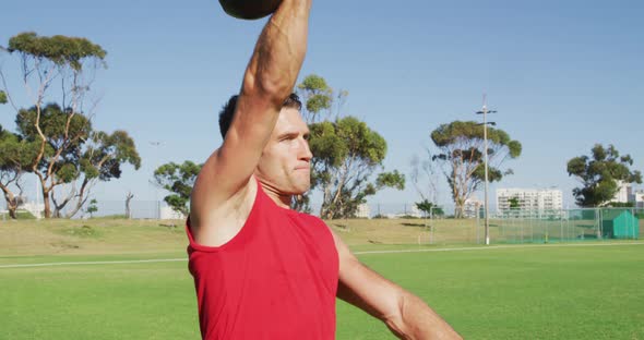 Fit caucasian man exercising outdoors, squatting and lifting kettlebell weight with one arm alt