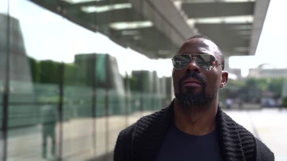 Confident Afro-american Man Is Walking at City, Wearing Sunglasses, Looking Around alt