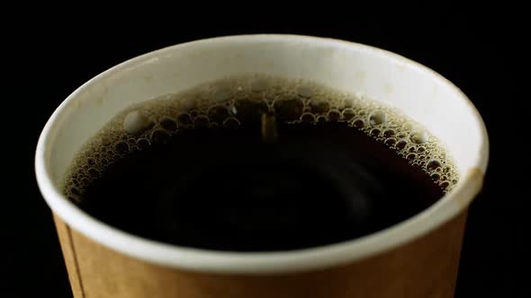 Small drops slowly drip into a cup of freshly brewed coffee. Cup of coffee on a black background
