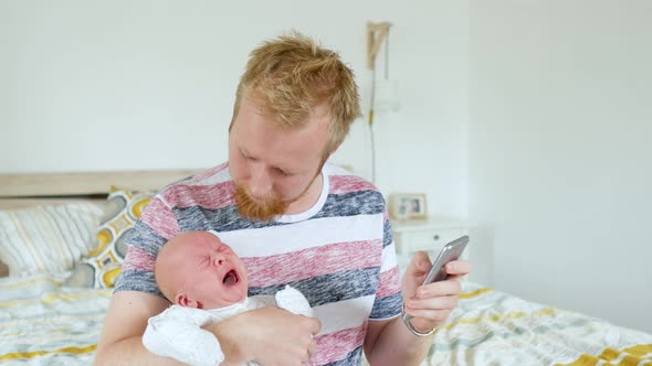 a man with a crying baby in his arms looking for information on the phone