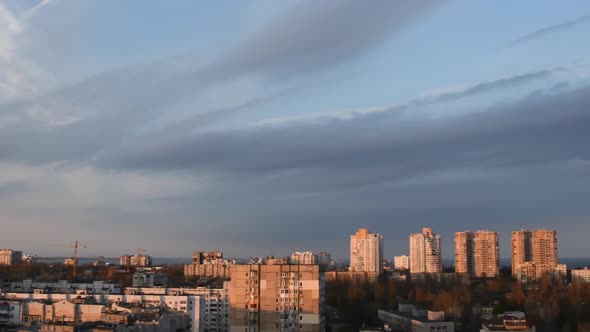 Grey Spindrift Clouds in Blue Sky Over Cityscape in Golden Hour of Sunset