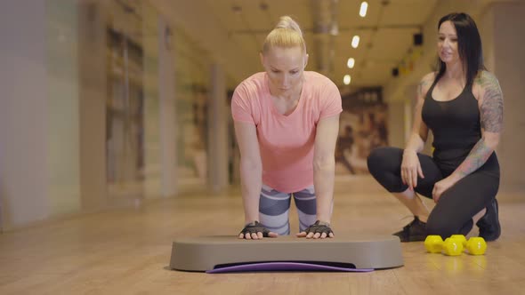 Professional Personal Trainer Controls Workout of Athletic Woman in Gym. Tattooed Caucasian Woman alt