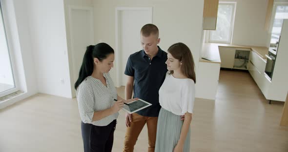 Estate Agent Showing Young Couple Around New House With Digital Tablet alt