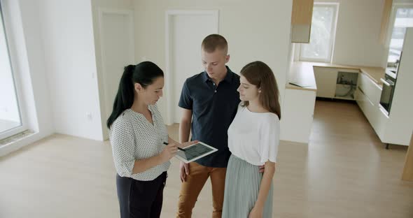 Estate Agent Showing Young Couple Around New House With Digital Tablet