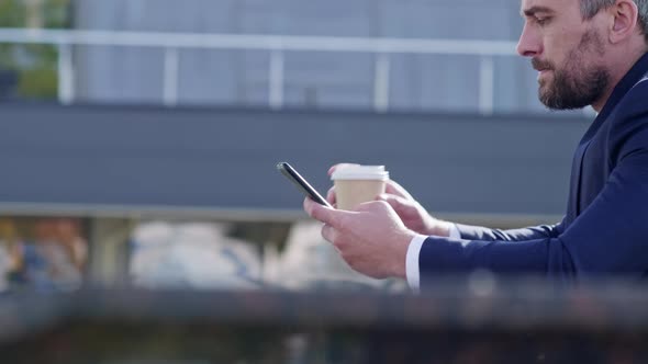 Businessman drinking coffee and using smartphone on the street