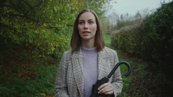 Young Woman In Coat And Carrying Umbrella