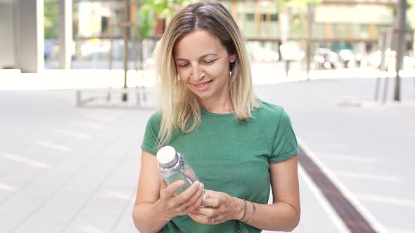 Blond woman standing in city showing bottle with clear water