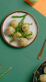 Vertical Flat Lay Video the Cook Puts Plate of Cooked Potato Dumplings with Baked Asparagus