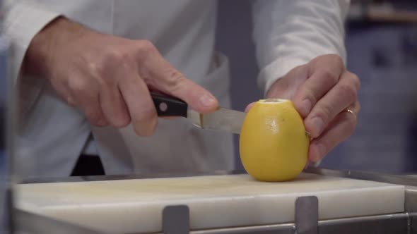Chef uses a knife to cut the lemon in half. The lemon has seeds inside.