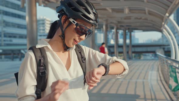 Asian businesswoman with backpack bicycle smil look smartwatch in city street go to work at office.