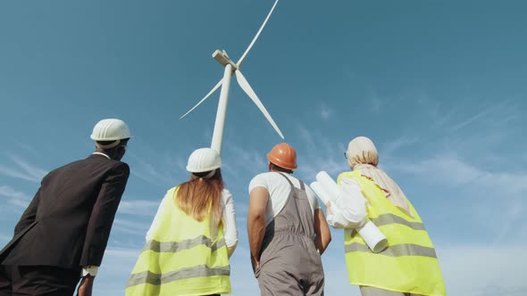 Back View of Men and Women in Uniform and Safety Helmets Looking on Huge Wind alt