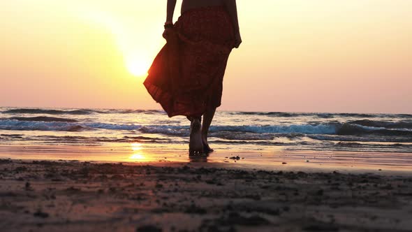 Young Woman Walking Barefoot Toward the Sea at Beautiful Sunset Rear View
