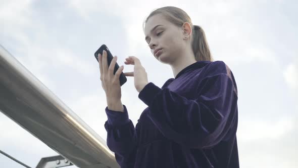 Bottom View of Young Surprised Woman Looking at Smartphone Screen and Gasping alt