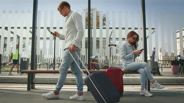 A Young Woman is Sitting at a Public Transport Stop and Texting on Her Smartphone alt