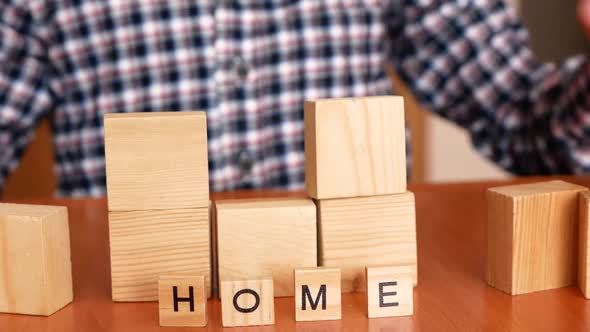 Close-up of a child's hand building a house from wooden cubes alt