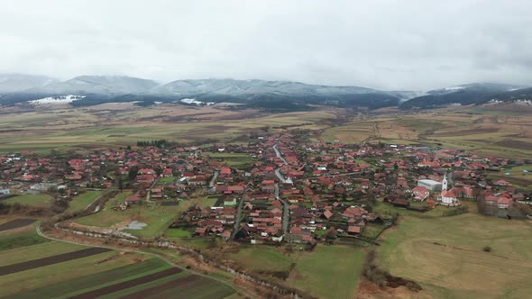 Flyover above homes, buildings of Sancraieni, Romania. Ciuc Mountains in background alt