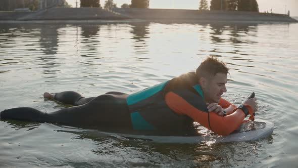 Man Lying and Smiling on a Surfboard Wearing Wetsuit at Warm Golden Sunset alt
