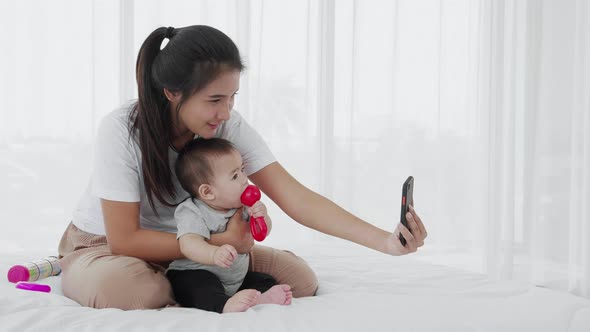 mother take care her baby while use smartphone to call on bed, Slow motion