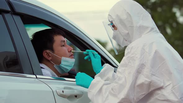 doctor in PPE suit test coronavirus(covid-19) to man in car by nasal swab cotton, drive thru test