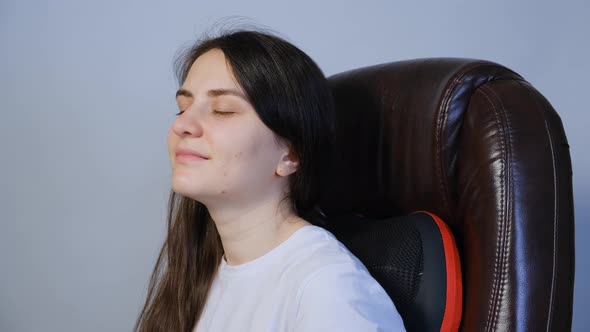 A Woman Sits in a Chair with a Massage Pillow and Massages Her Back alt