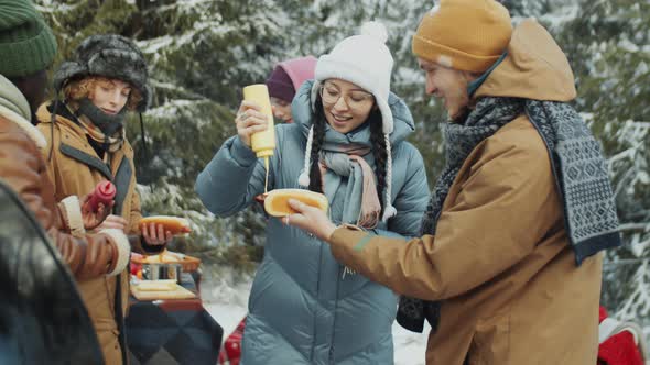 Friends Making Hot Dogs on Winter Picnic in Forest alt