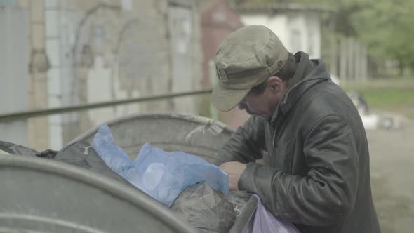 A Beggar Homeless Man Tramp Is Looking for Food in a Trash Can. Kyiv. Ukraine alt