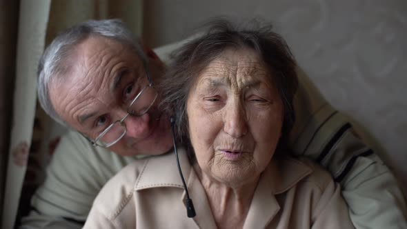 Very Old Woman in Headphones Making Video Conversation on the Phone in Their Home alt