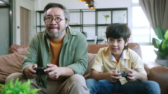 asian dad son play video game together at home fun and excited hand hold joystick